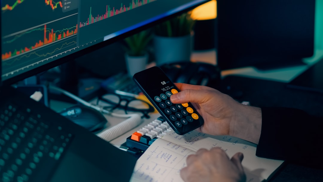 Financial trading workstation stock crypto investment analysis. Closeup hand holding phone calculator desk monitors candlestick graphs market data savings portfolio planning risk management economy finance technology office night lighting focus strategy performance growth profit volatility currency bitcoin ethereum exchange dashboard indicators keyboard notebook calculations